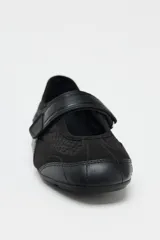 Zapato tipo bailarina color negro, con capellada de cuero sintético y rejilla. Tiene tira con velcro en el empeine y suela plana.