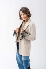 Blazer color beige con solapas de muesca, cierre frontal con un botón y bolsillos de parche. Las mangas largas están adornadas con plumas negras.