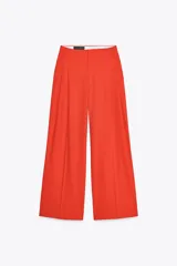 Pantalón de vestir color naranja, de tiro alto y pernera ancha. Presenta doble pliegue frontal, trabillas en la cintura, bolsillos laterales y falsos bolsillos de vivo en la espalda.