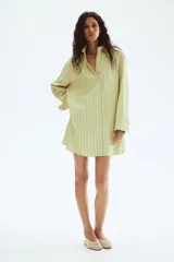 Vestido camisero de manga larga, color verde claro con finas rayas verticales oscuras. Presenta cuello de pico, botonadura frontal y corte evasé/oversized.