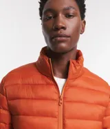 Campera puffer ultraligera color beige, con cuello alto, cierre por cremallera y bolsillos con cremallera. Incluye bolso de almacenamiento.