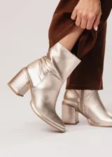 Bota de caña media color champagne de cuero, con horma redonda, taco cuadrado y pequeña plataforma. Cuenta con cierre del lado interno.