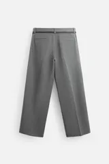 Pantalón gris de corte ancho con pliegues frontales y cinturón fino negro.
