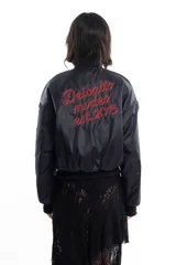 Campera bomber negra de tela satinada con cierre frontal, cuello redondo y puños y cintura elastizados. Tiene un pequeño logo bordado en el pecho y un bolsillo con cierre en la manga. Es reversible.