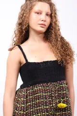 Top con parte superior de crochet negro y parte inferior de tejido plano de telar con diseño a cuadros en tonos amarillo, rojo y negro.