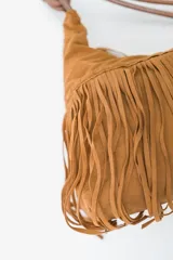 Bolso de hombro tipo hobo color rojo oscuro, confeccionado en material tipo gamuza o nobuk, con flecos largos en la parte inferior. La correa es delgada y se anuda en la parte superior.