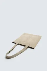 Bolso tipo shopper fabricado en piel con acabado serraje color gris oscuro. Tiene compartimento principal abierto con un bolsillo interior con cierre. Cuenta con dos asas de mano fabricadas en piel.