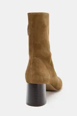 Botín de serraje color marrón, con tacón ancho en bloque y punta redonda. Presenta un detalle de pespunte en el cuerpo y cierre mediante cremallera lateral.