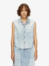 Camisa sin mangas de denim con lavado ácido, cuello camisero y cierre frontal de botones oscuros. Presenta un pequeño pin o aplique en la solapa izquierda.