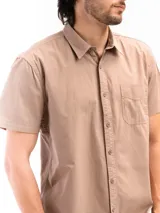 Camisa de manga corta color beige, confeccionada en 100% algodón, con cuello clásico, cierre frontal con botones y bolsillo en el pecho.