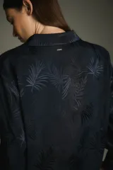 Pijama de satén jacquard azul con estampado de hojas de palmera, compuesto por una camisa de manga larga con botones forrados y un pantalón recto con cintura elastizada.