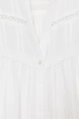 Camisa blanca de escote pico y manga larga con puños elásticos. Detalle de puntilla combinada a tono y cierre frontal con botones.