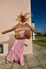 Sweater tejido de lana color marrón con bordado de flores y texto 'CACAU' en color rosa. De calce holgado, cuello redondo y puños ajustados.