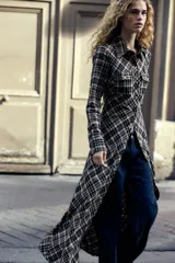 Vestido largo tipo camisero con estampado de cuadros en tonos marrón, negro y blanco. Tiene cuello solapa, mangas largas con puños abotonados, dos bolsillos de parche con solapa en el pecho y cierre frontal con botones a presión.