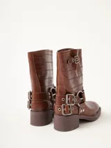 Botas cortas de cuero marrón con textura, hebillas ajustables, apliques circulares y punta cuadrada.