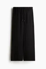 Pantalón negro de piernas anchas con bolsillos laterales, cintura elástica y cordón de ajuste con cuentas decorativas en los extremos.