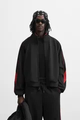 Chaqueta negra con detalles en rojo, cuello alto, cierre frontal con cremallera, bolsillos laterales y puños elásticos.