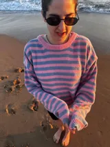 Sweater de tejido de punto con rayas horizontales anchas en tonos rosa claro y celeste/azul pálido. Presenta un corte holgado y cuello redondo.