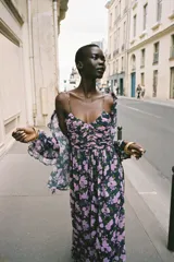 Vestido largo negro con estampado floral en tonos lila y verde. Escote en pico, tirantes finos, detalle drapeado en el busto, forro interior y cierre lateral con cremallera oculta.