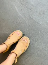 Sandalias de cuero color beige con tiras entrecruzadas y hebilla lateral.