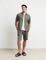 Camisa sport de manga corta color verde oliva, línea premium, con cuello clásico, cierre frontal con botones de coco y bolsillo de parche en el pecho. Confeccionada en lino y algodón.