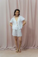 Blusa blanca de lino con escote en V, mangas cortas abullonadas y cierre frontal con lazos.