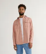 Camisa overshirt color salmón de sarga de algodón con capucha gris ajustable con cordones. Tiene cierre frontal con botones, dos bolsillos con solapa en el pecho y mangas largas con puños abotonados.