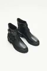Bota de cuero negra con caña media, tiras cruzadas con hebillas y remaches metálicos, laterales matelaseados y cierre lateral interno.