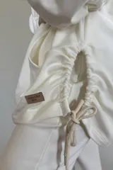 Canguro oversize color blanco, con capucha, cordones ajustables, mangas 3/4 con puños elásticos, bolsillos laterales y ruedo irregular con cordones ajustables.