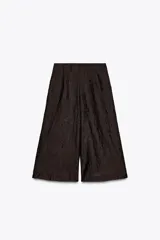 Pantalón culotte color marrón oscuro, de tiro alto con pliegues delanteros y tejido semitransparente efecto arrugado. Tiene forro interior y cierre lateral con cremallera oculta.