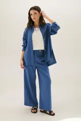 Pantalón de lino azul de corte palazzo con botón decorativo en la cintura.