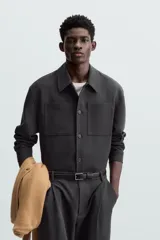 Sobrecamisa negra de corte amplio, con cuello solapa, manga larga con puños abotonados, bolsillos de parche en el pecho, bolsillos laterales y cierre frontal con botones.