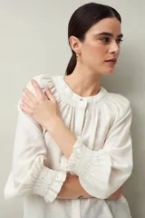 Camisa color crema de lino con cuello redondo, canesú fruncido, mangas largas amplias con puños elastizados con volado y cierre frontal con botones.