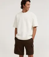 Bermuda masculina color marrón oscuro, confeccionada en tela French Terry, con cintura elástica y cordón de ajuste. Presenta bolsillos cargo funcionales a los lados.