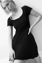 Vestido mini negro de manga corta en punto de algodón acanalado con pollera evasé. Modelo con cuerpo entallado y escote redondo amplio con ribete fino blanco y moña decorativa de satén. Ribete sobrehilado en mangas y bajo.