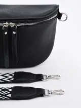 Riñonera negra de cuero con forma curva y cierre superior de cremallera metálica plateada. Presenta tiradores de cuero colgantes en los cursores y anillas metálicas a los lados para sujetar la correa.