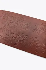 Cinturón tipo fajín de cuero color marrón con detalle de flores labradas. Cierre ajustable con lazada en el mismo material.