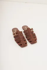 Sandalias planas de cuero color marrón con diseño de tiras entrecruzadas y hebilla lateral ajustable.