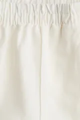 Pantalón blanco de lino con cintura elástica, bolsillos al bies y bolsillos traseros insertados. Piernas rectas con pliegue cosido adelante.