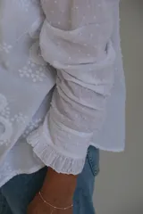 Camisa blanca con bordado floral, cuello mao y mangas largas con puños elásticos.