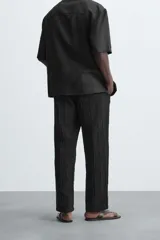 Pantalón negro de corte amplio, con textura acanalada, cintura elástica ajustable con cordón, bolsillos laterales y traseros de vivo.