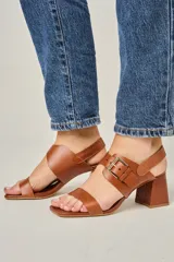 Sandalias de cuero color champagne, con punta cuadrada, tira ancha sobre el empeine y tira al tobillo con hebilla metálica. Taco cuadrado de 7 cm.