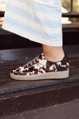 Zapatillas bajas con capellada de pelo de vaca color marrón y blanco, con cordones finos color beige y suela de goma color beige.