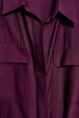 Vestido camisero midi color morado oscuro, con cuello solapa, manga corta y bolsillos de plastrón con solapa en el pecho. Incluye un cinturón ancho del mismo tejido anudado a la cintura.