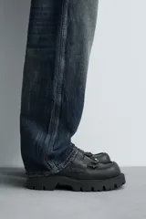 Mocasín negro con flecos. Parte superior lisa con efecto desgastado. Detalle de antifaz y flecos con puntas metálicas en el empeine. Horma cuadrada. Suela con volumen.