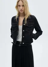 Chaqueta de jean azul oscuro con cuello camisero, cierre frontal abotonado, mangas largas con puños abotonados, dos bolsillos con solapa en el pecho y costuras decorativas. Confeccionada en tejido de algodón.