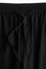 Pantalón negro de corte holgado en algodón, con tiro alto, cintura elástica fruncida y cordón para ajustar. Piernas anchas con bolsillos laterales.
