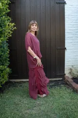 Vestido largo color cereza, con mangas amplias y escote en V. Presenta múltiples capas de tela con terminaciones deshilachadas, creando un efecto voluminoso y vaporoso.