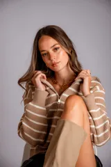 Sweater de punto color beige con rayas horizontales blancas, cuello polo con cierre de cremallera y mangas largas.