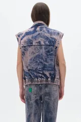 Chaleco de jean azul con lavado ácido y detalles en rosa, de corte oversize y sin mangas.